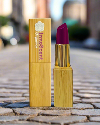 Beetroot Bliss Lipstick in eco-friendly, refillable bamboo packaging, displayed on a textured rock floor in an urban city setting. The rich beetroot red hue contrasts with the rugged city landscape, reflecting a bold, natural beauty with a modern edge.