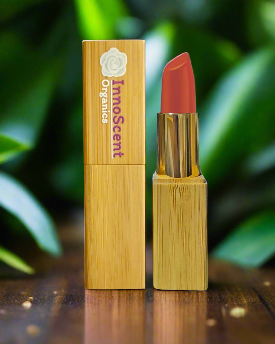 Dahlia Dream Lipstick in eco-friendly, refillable bamboo packaging, placed on a rich walnut table. The deep, floral pink hue of the lipstick contrasts beautifully with the warm wood tones, highlighting its elegant, natural appeal.