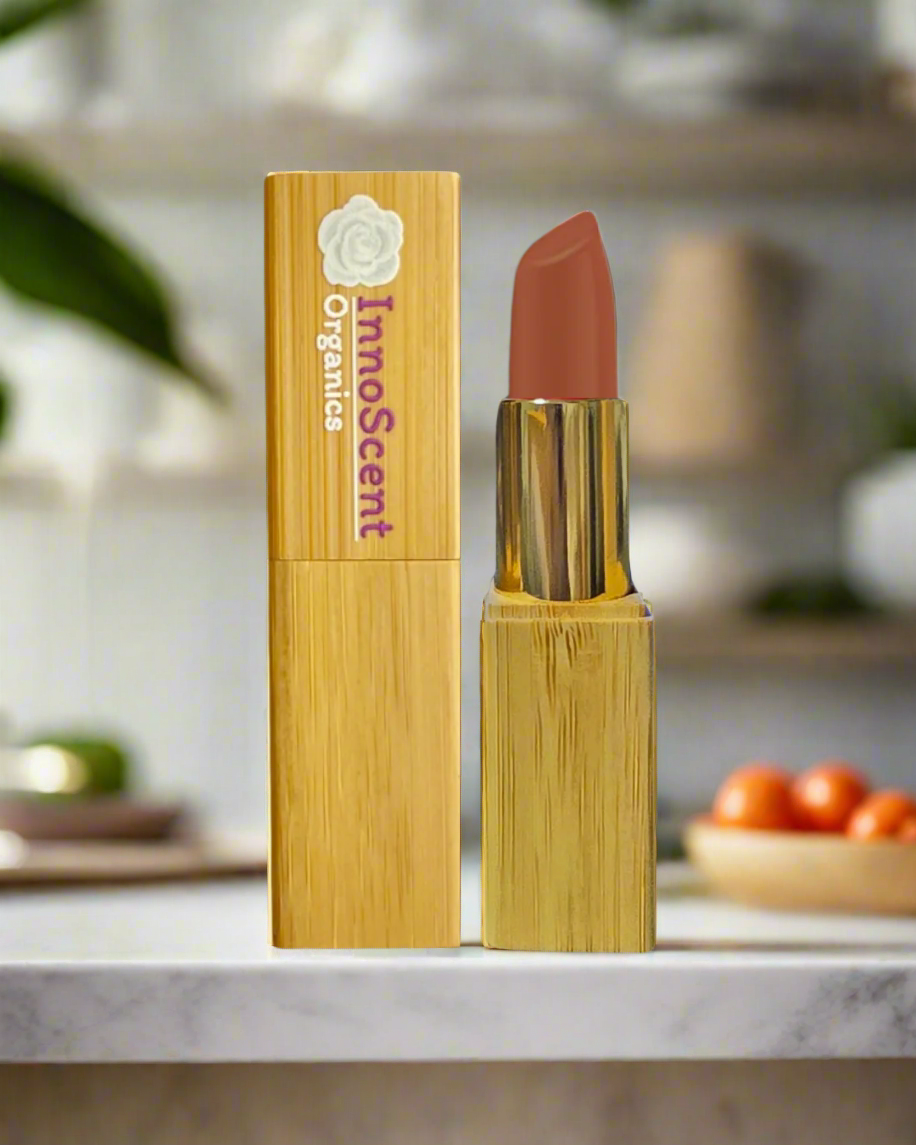 Honey Glow Lipstick in eco-friendly, refillable bamboo packaging, placed on a sleek marble floor in a kitchen setting. The warm, golden honey shade of the lipstick complements the smooth marble surface, with a ripe tomato subtly featured in the background, adding a touch of freshness and natural vibrancy to the scene.