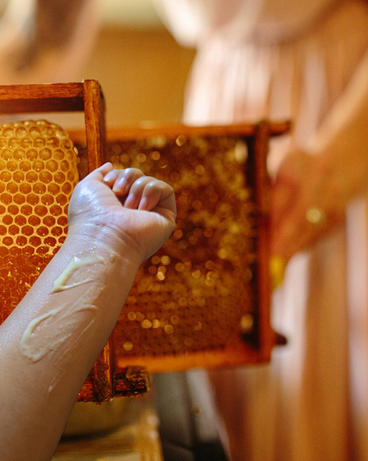 Person applying propolis serum onto their skin, with a honey bee farm in the background, symbolizing the natural origin and purity of the ingredients.