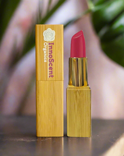 Raspberry-colored lipstick in refillable bamboo packaging, showcased against a lush jungle background with an eco-friendly icon, highlighting its natural and sustainable beauty.