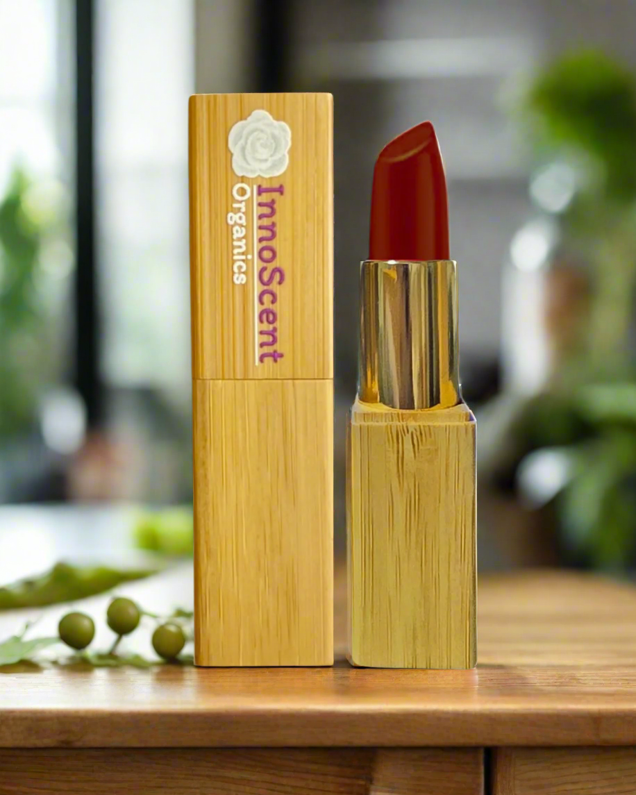 Tomato Red Lipstick in eco-friendly, refillable bamboo packaging, displayed on wood table in a cozy kitchen setting. The vibrant red hue of the lipstick mirrors the rich color of fresh tomatoes, adding a bold pop of color against the natural warmth of the wood.